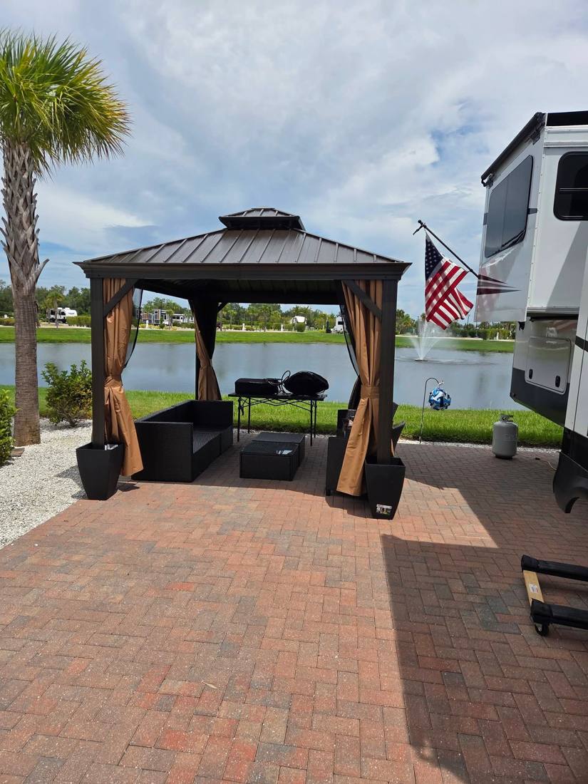 Brown hardtop gazebo with curtains on a paver patio by a lake